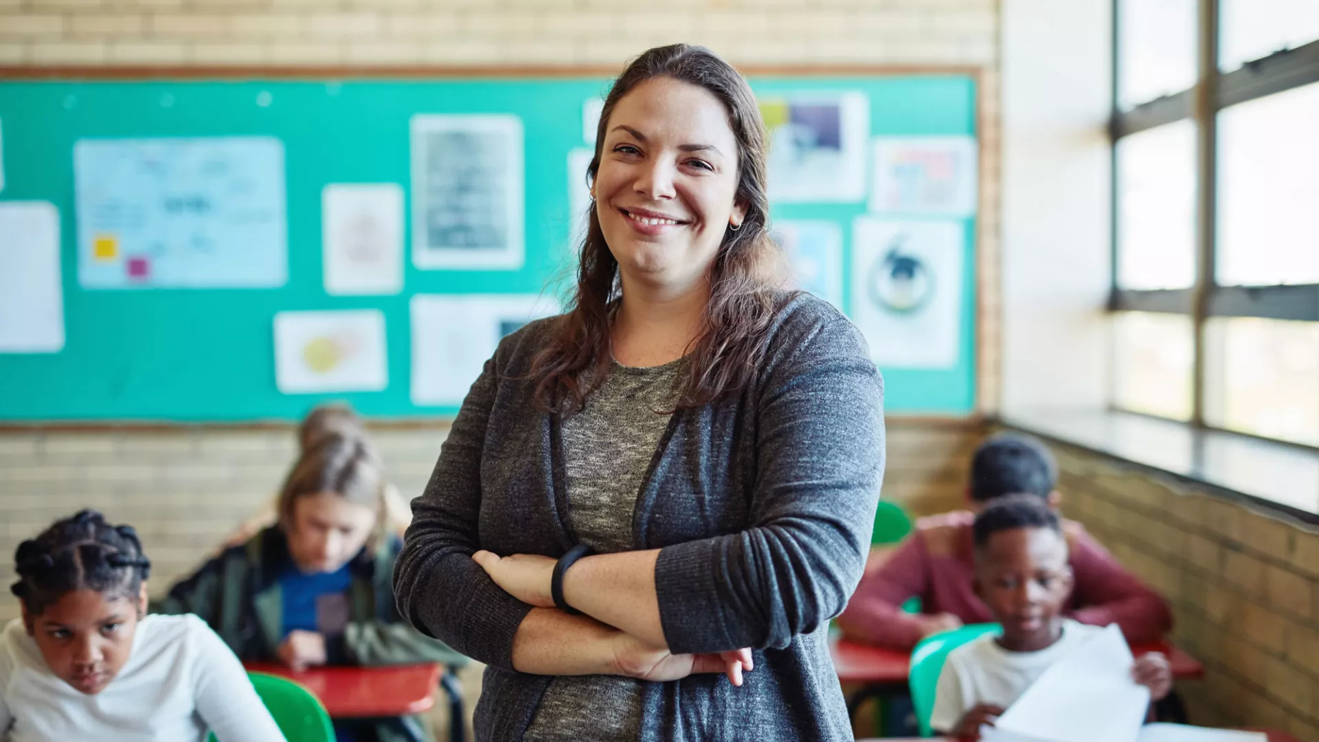 a teacher looks into the camera with her students in the background