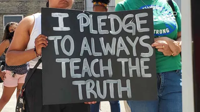 Two women carry a "I Pledge to Teach the Truth" poster at a march